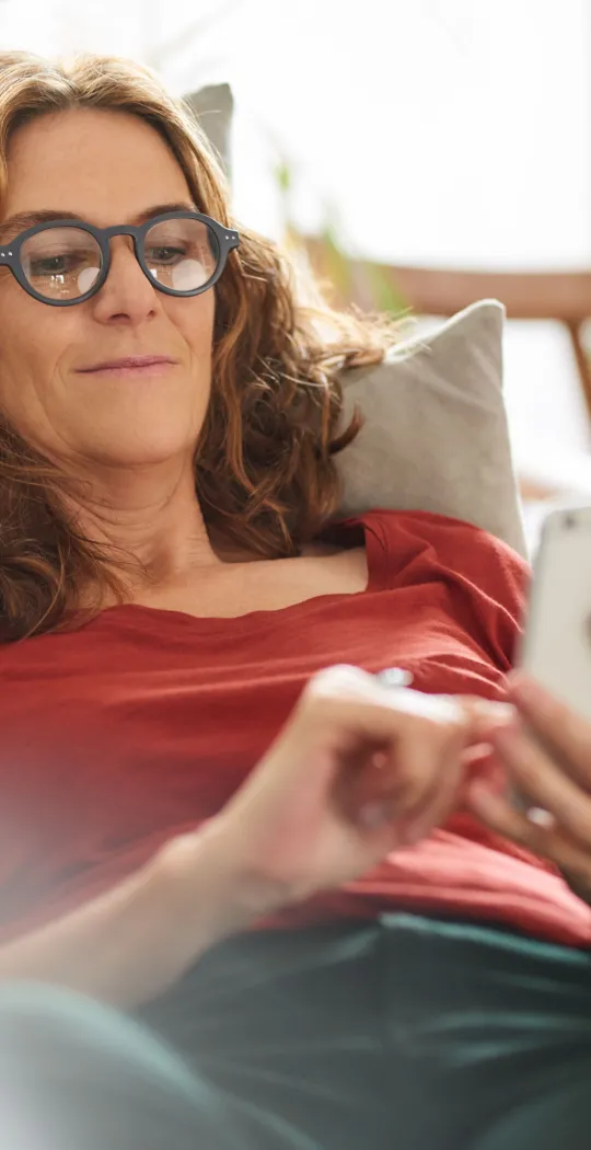 Frau liegt mit Smartphone auf Couch