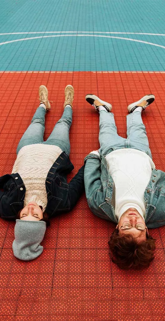 Junges Paar liegt auf dem Boden eines Sportplatzes.